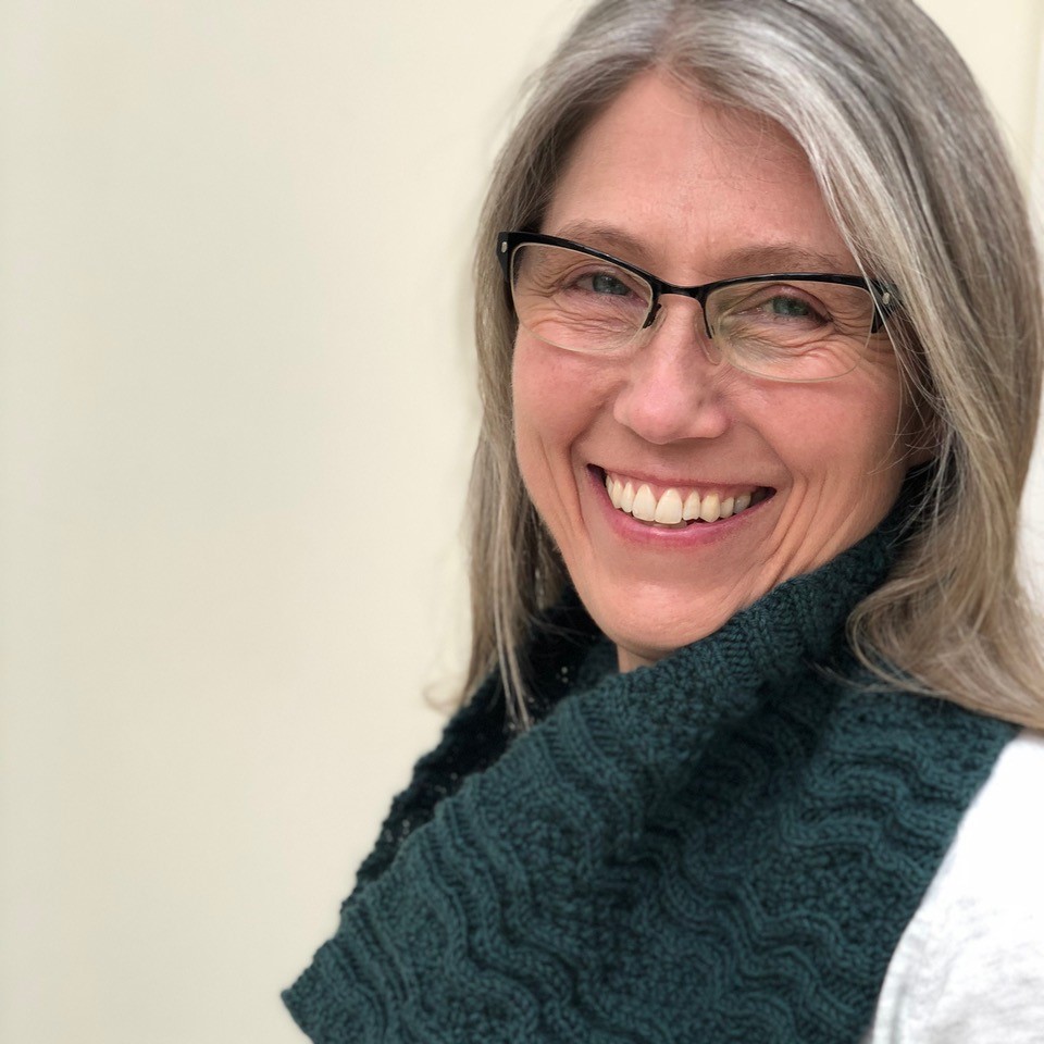 A headshot of Emma Vining in her green handknitted cowl