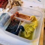 3 plastic tubs with sections of a warp draped into the blue, orange and yellow dyes
